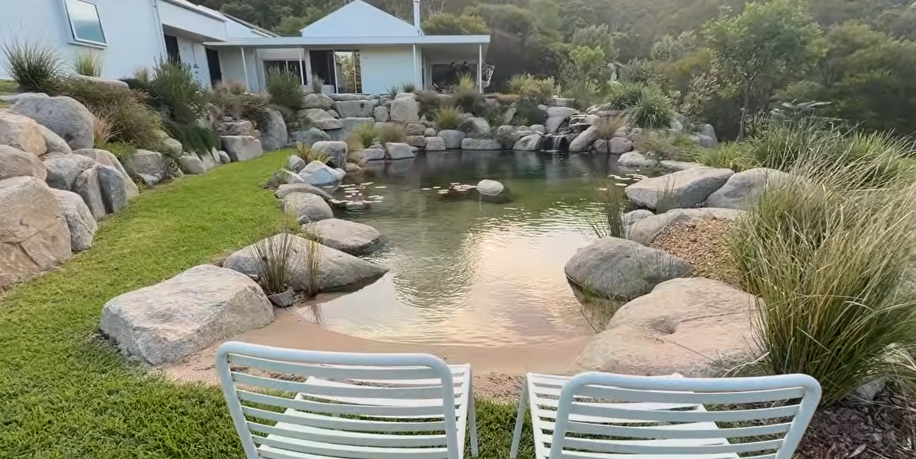 Referência visual de lago integrado ao jardim, com bordas de pedra, vegetação e profundidades variadas